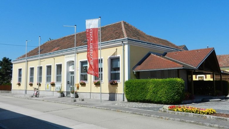 Gemeindeamt in Rauchenwarth, gelbes Gebäude mit rotem Dach und Blumen.