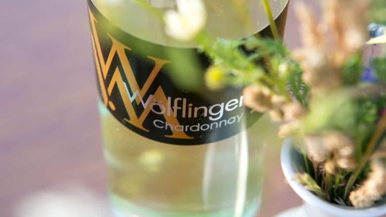 Nahaufnahme einer Weinflasche mit der Aufschrift 'W&ouml;lflinger Chardonnay' neben einem Blumenstrau&szlig;.