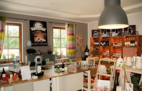 Innenansicht eines Hofladens mit Regalen voller Weinflaschen und Produkten.