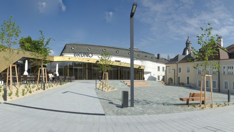 Moderne Architektur mit goldener Fassade und traditionellem Geb&auml;ude im Hintergrund, blauer Himmel.