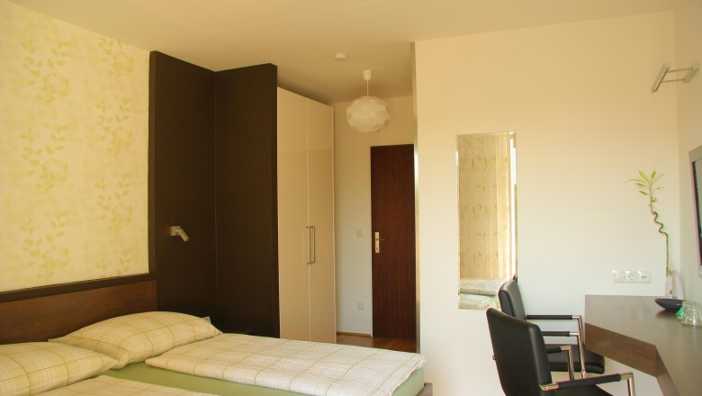 Ein modernes Hotelzimmer mit zwei Einzelbetten, einem Schreibtisch und einem Stuhl. Die W&auml;nde sind hell und mit einem Pflanzenmuster dekoriert.