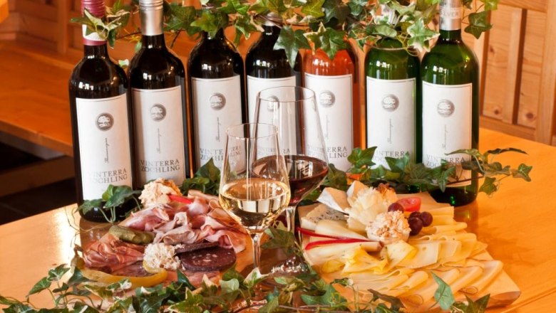 Weinflaschen und kalte Platten mit K&auml;se und Wurst auf einem Tisch.