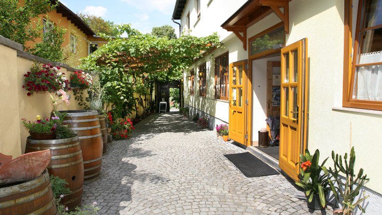 Eingang eines Heurigen mit gelben Türen, Pflastersteinen und Pflanzen.