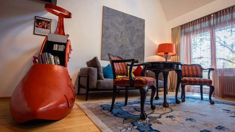 A stylishly furnished hotel room with a large red shoe as a bookshelf, antique chairs, a table and a floor lamp.