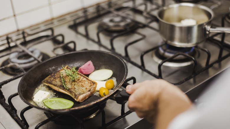 A pan with fish, vegetables and herbs on a stove.