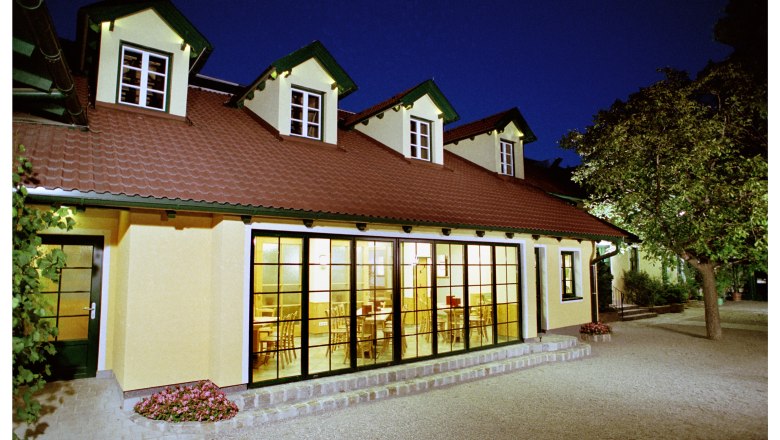 Ein Geb&auml;ude mit gelber Fassade und roten Dachziegeln bei Nacht, beleuchtet von innen.