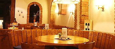 Gem&uuml;tliches St&uuml;berl mit Holztisch und St&uuml;hlen, umgeben von rustikalen Backsteinb&ouml;gen und warmem Licht.