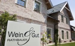 Ein Schild mit der Aufschrift 'Wein & Gut Rathbauer' vor einem Backsteingeb&auml;ude.