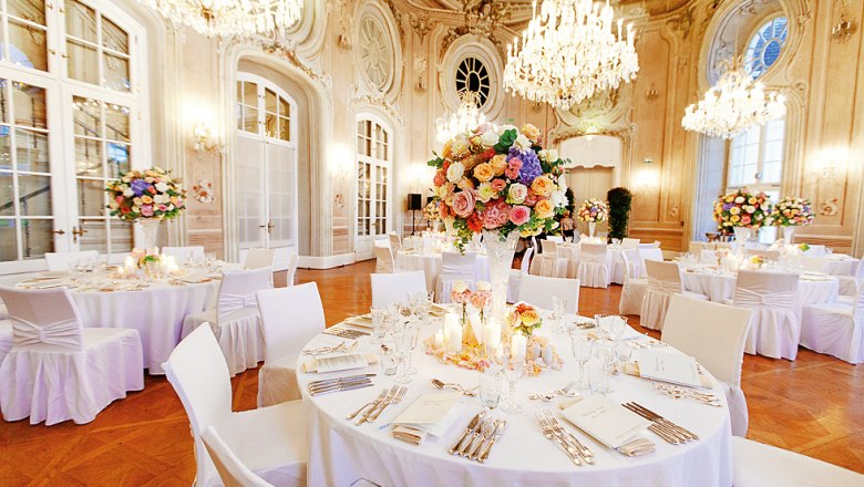 Elegant banquet hall with round tables, flower arrangements and chandeliers.