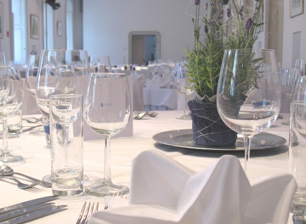 Elegant table with white tablecloth, glasses, cutlery and lavender decorations in a festive room.