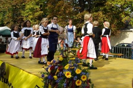 Kinder in Trachten tanzen auf einer Bühne im Freien.