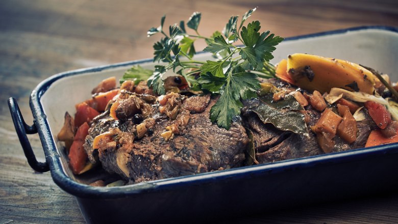 A roast with vegetables and herbs in a casserole dish.