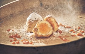 Eismarillenknödel mit Puderzucker und Aprikosensauce auf einem Sieb.