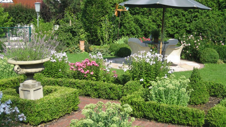 Ein gepflegter Garten mit Blumenbeeten, einem Sonnenschirm und Sitzbereich.