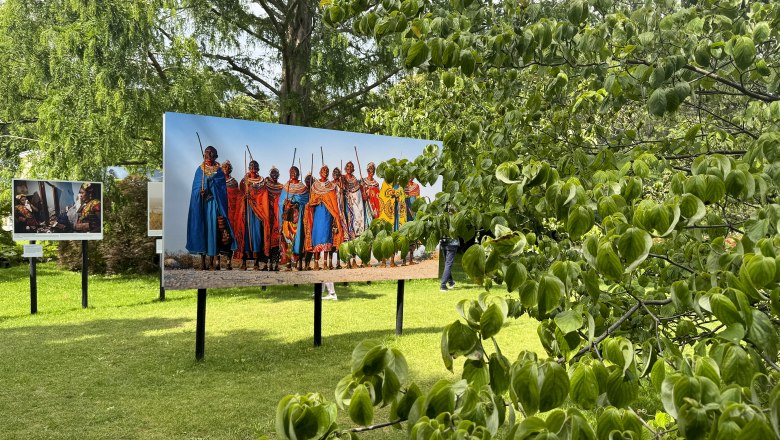 Outdoor photo exhibition with pictures of people in traditional clothing on a meadow.