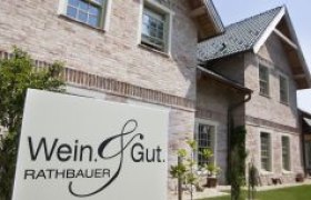 Ein Schild mit der Aufschrift 'Wein & Gut Rathbauer' vor einem Backsteingeb&auml;ude.