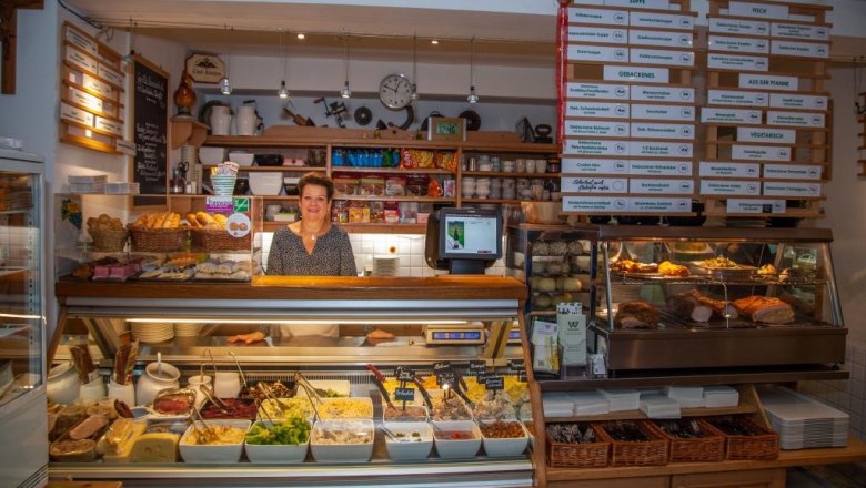 Frau hinter einem Buffet mit verschiedenen Speisen in einem Restaurant.