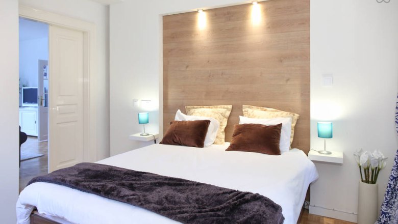 Modernes Schlafzimmer mit Doppelbett, Holzr&uuml;ckwand und blauen Nachttischlampen.