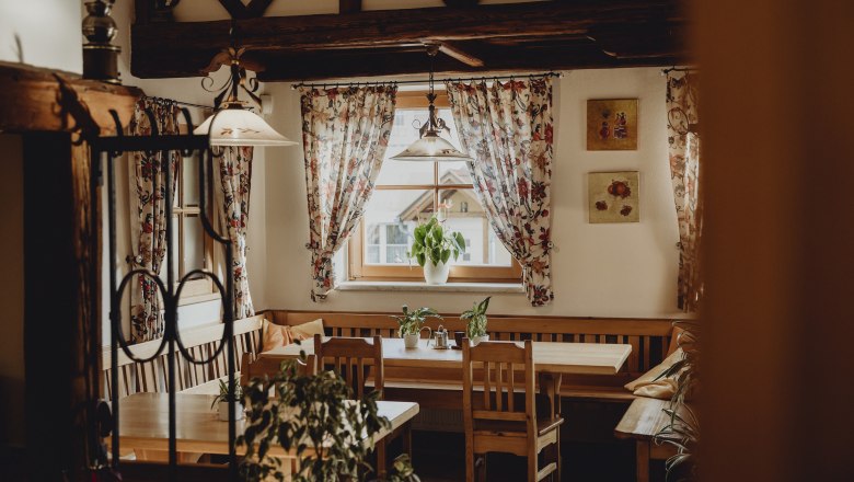 Gem&uuml;tlicher Raum mit Holzm&ouml;beln, Pflanzen und gebl&uuml;mten Vorh&auml;ngen.