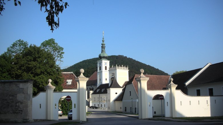 Eingangstor des Stifts Heiligenkreuz mit Kirchturm im Hintergrund.
