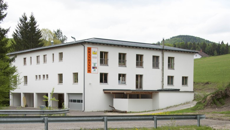 Ein wei&szlig;es Geb&auml;ude mit der Aufschrift 'Brandtner' in l&auml;ndlicher Umgebung.