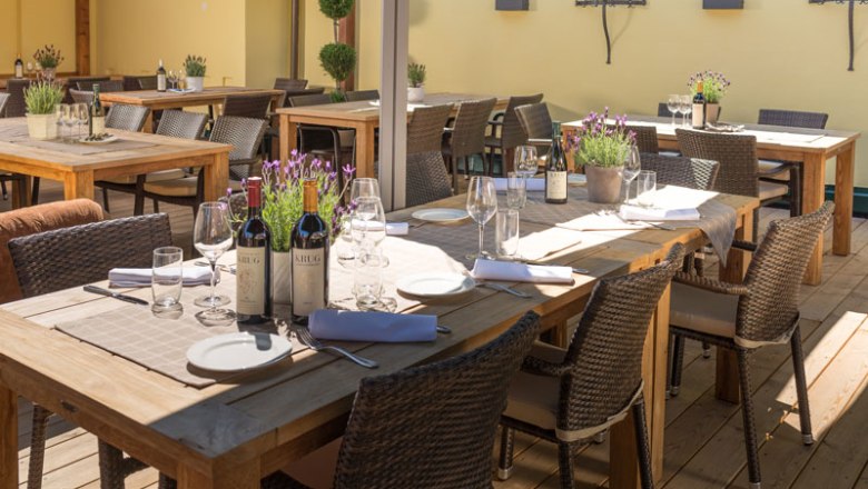 Eine Terrasse mit Holztischen, gedeckt mit Weinflaschen, Gläsern und Lavendel in Töpfen.