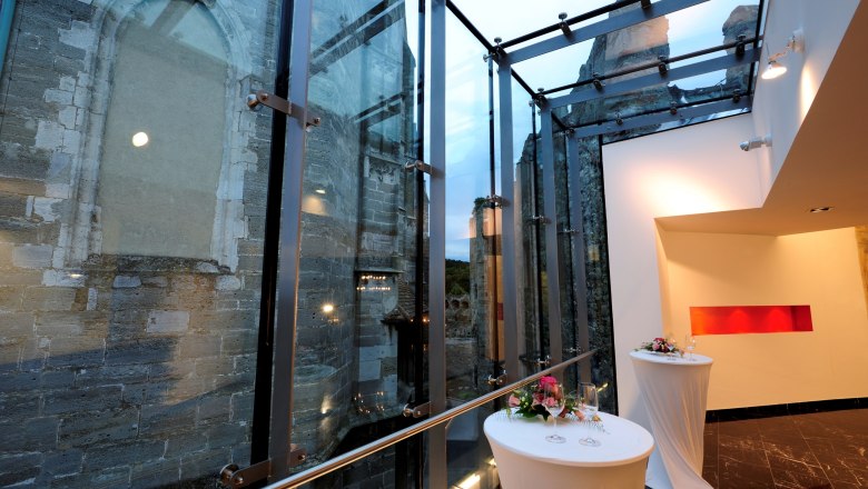 Modern glass architecture next to an old stone wall with decorated bar tables.