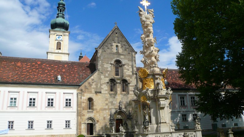 Innenhof des Stifts Heiligenkreuz mit barocker Säule und Kirchturm.