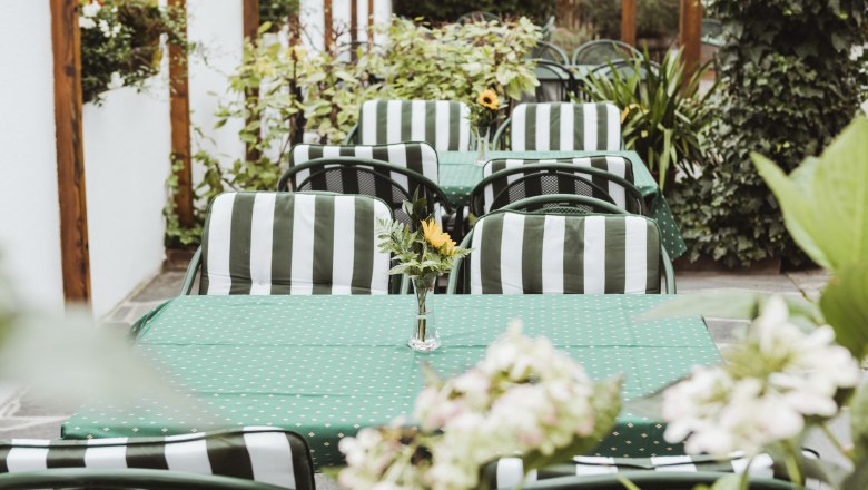 Ein gem&uuml;tlicher Au&szlig;enbereich mit gr&uuml;n-wei&szlig; gestreiften St&uuml;hlen und gr&uuml;nen Tischdecken, dekoriert mit Blumenvasen.