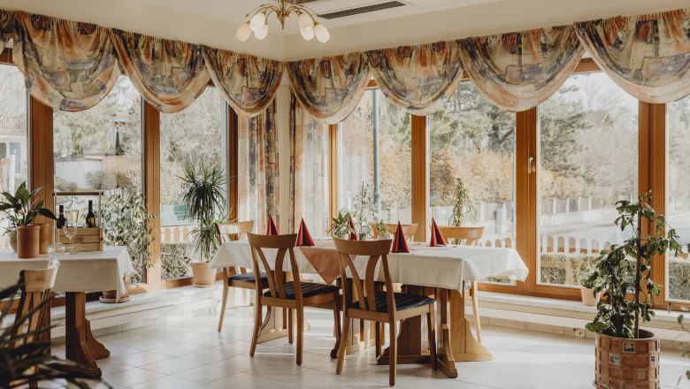 Ein helles Restaurant mit gro&szlig;en Fenstern, Holzm&ouml;beln und Pflanzen.