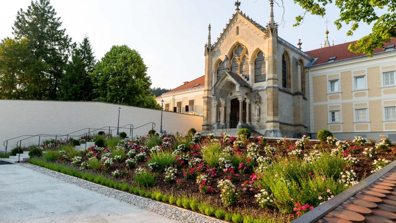 Eine Kirche mit gotischen Elementen und einem gepflegten Garten voller Blumen im Vordergrund.