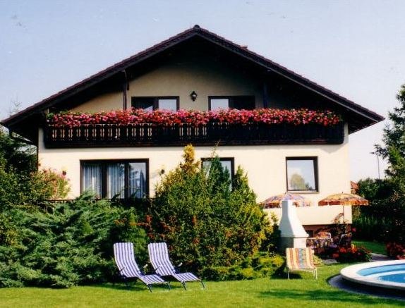 Zweist&ouml;ckiges Haus mit Balkon, Gartenm&ouml;beln und Pool im Vordergrund.