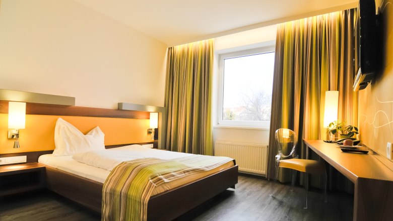 Modernes Hotelzimmer mit Doppelbett, Schreibtisch und großem Fenster.