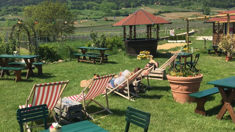 Garten mit Liegestühlen und Tischen, im Hintergrund Hügel und blauer Himmel.