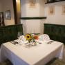 Cozy restaurant corner with green tiled stove, table setting and flowers.