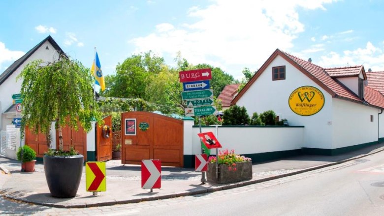 Eingang zum Weingut Wölflinger mit Schildern und Pflanzen.