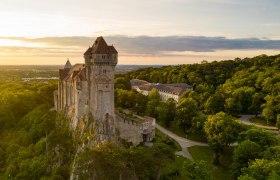 Burg Liechtenstein auf einem Hügel, umgeben von Wald, bei Sonnenuntergang.