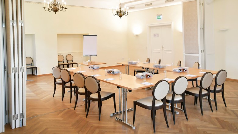 Conference room with tables and chairs, flipchart and chandelier.