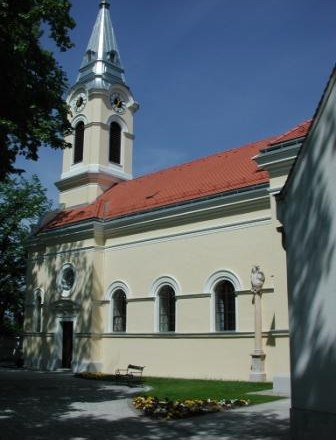 Pfarrkirche Tattendorf mit gelber Fassade und rotem Dach, umgeben von Bäumen.