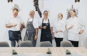 Fünf Personen in Kochkleidung lachen und halten Weingläser in der Hand.