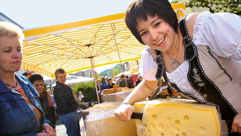 Frau in traditioneller Kleidung schneidet K&auml;se auf einem Markt.