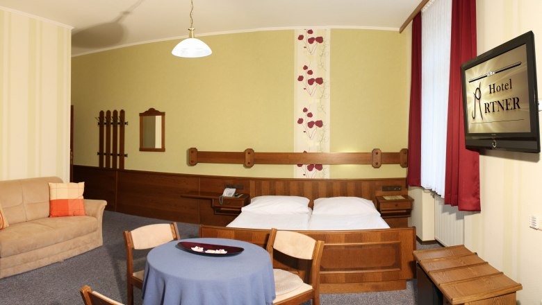 Hotelzimmer mit Doppelbett, Sofa, Tisch und Fernseher.