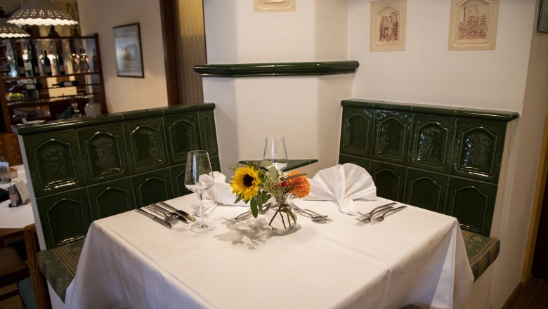 Cozy restaurant corner with green tiled stove, table setting and flowers.